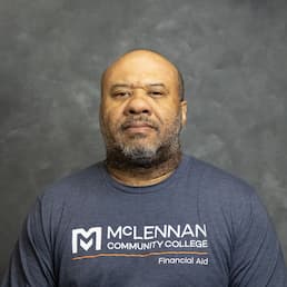 Man wearing a McLennan Community College Financial Aid T-shirt against a gray background.